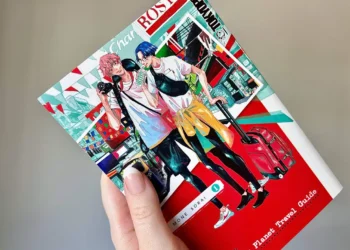 A hand holding volume 1 of the manga Our Not So Lonely Planet Travel Guide