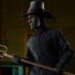 The John Carver Sixth Scale Figure wears a burned mask and pilgrim hat while wielding a pitchfork